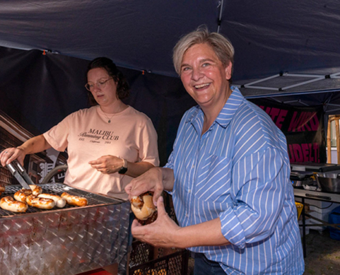 Melanie Witte-Lonsing hilft an einem Grillstand und bereitet ein Wurstbrötchen vor.